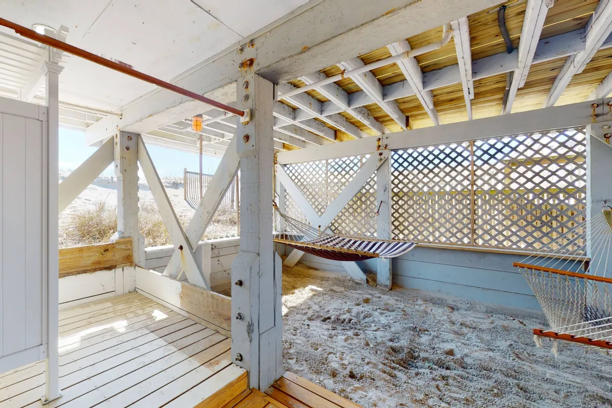 A cozy hammock area set beneath wooden beams, resting above a sandy floor. The tranquil nook invites quiet relaxation, reading, or an afternoon nap, with the gentle island breeze drifting through. The scene feels intimate and sheltered, perfect for unwinding after a day by the shore.