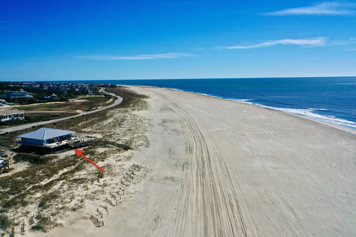 This image captures a sweeping view of a beachfront property fronting an expansive, sandy beach with rolling ocean waves. The openness of the shoreline, bright sky, and visible proximity of the house to the sand evoke a sense of direct beach access and ample space for family games, sandcastle building, and beach strolls.
