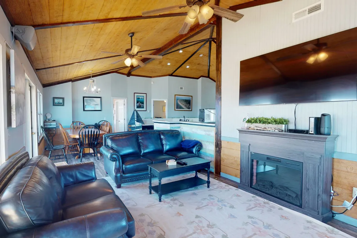 A welcoming interior space featuring a leather sofa positioned for relaxation, a large dining table that can seat multiple guests, a cozy fireplace, and a Smart TV. Natural light pours in through windows, creating a comfortable, communal atmosphere ideal for group gatherings or family meals.