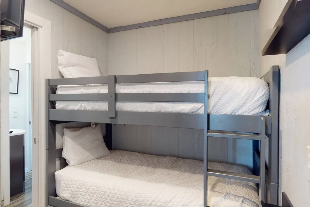 A cozy, inviting bunk room with double twin bunk beds, soft pillows, and textured walls, designed for children or young guests to share laughter and stories.