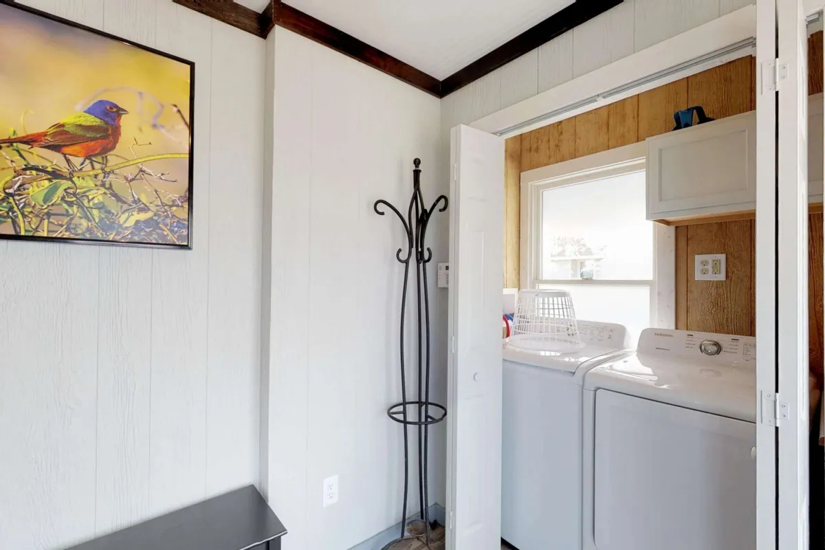 A cheerful and functional laundry space featuring modern appliances, a coat rack, and bird-themed artwork on the wall. The design is practical, easy to clean, and inviting, ideal for active beachgoers and families with pets.